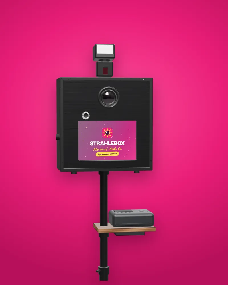 Die STRAHLEBOX-Fotobox mit schwarzer Holzfront, Canon-Kamera, Touchscreen, Blitz und Drucker auf der Holzablage